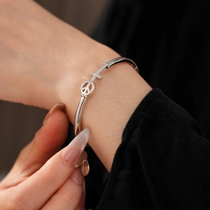 Detailed close-up of a silver-toned bangle featuring a peace symbol and zircon cross