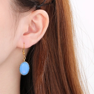 Macro shot of blue oval glass pendant earrings with gold hooks worn by a model