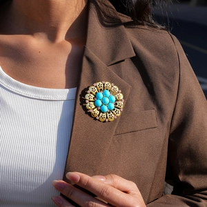 Close-up of a vintage hollow floral brooch with turquoise beads on a brown blazer