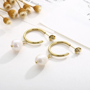 Détail de créoles en or 18K avec perle d'eau douce baroque sur un fond minimaliste