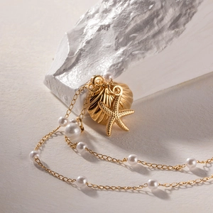 Detail of gold starfish and shell pendant necklace with white pearls on a textured stone