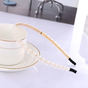 Elegant gold metal headband with white faux pearls displayed by a white coffee cup