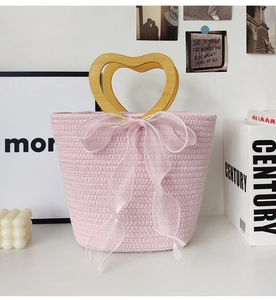Detailed view of pink woven handbag featuring heart-shaped wooden handle and soft gauze bow