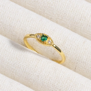 Macro shot of gold emerald ring with side stones on white knit fabric background