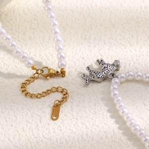 Macro detail of faux pearl necklace featuring a silver tiger pendant and gold extension chain