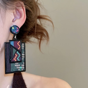 Close-up of retro drop earrings with colorful geometric woven fabric and black frame