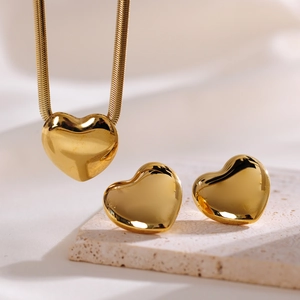 Detailed view of polished gold heart necklace and stud earrings set on stone