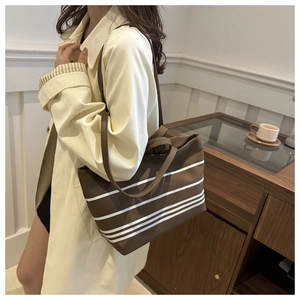 Close-up of brown striped canvas tote bag with leather handles held by a model indoors