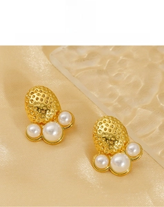 Detail view of strawberry shaped gold earrings with pearls on soft champagne silk fabric