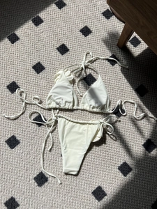 Detail of off-white bikini with 3D floral accent and side-tie briefs on textured rug