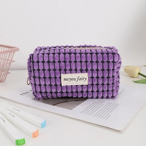 Close-up of deep purple waffle textured cosmetic bag with woven label on a desk