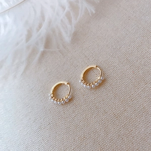 Macro detail of gold pearl hoop earrings on beige fabric with soft white feathers