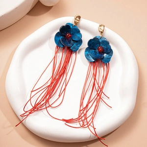 Détail de boucles d'oreilles à fleurs avec pétales bleus et franges en soie rouge sur céramique