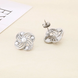 Detailed view of silver swirl flower earrings with white pearl inlay on a flat surface