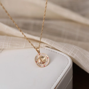Detailed close-up of a round gold pendant necklace with red and white enamel accents