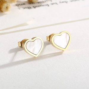 Macro detail of heart-shaped earrings with gold frame and white shell inlay on background