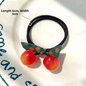 Detail of cherry hair tie with green polka dot bow, measuring 6cm by 3cm on a plate
