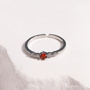Detail of four-prong set red ruby ring with side zircons on a white stone texture