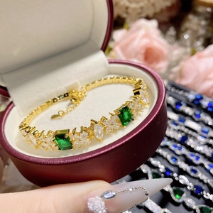 Detailed shot of camellia gold bracelet with green spinel and clear gems in a velvet box