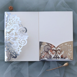 Macro view of beige wedding invitation featuring laser-cut silver lace patterns