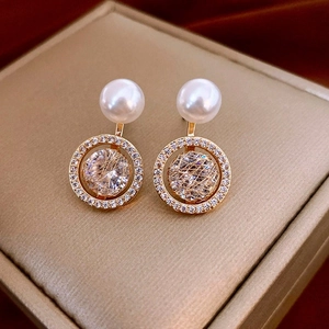 Macro detail of geometric pearl earrings with gold wire-wrapped crystals and pavé stones