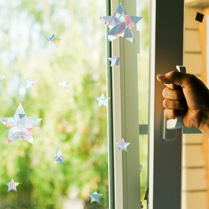 Hand opening a window featuring multiple holographic star-shaped prism window decals