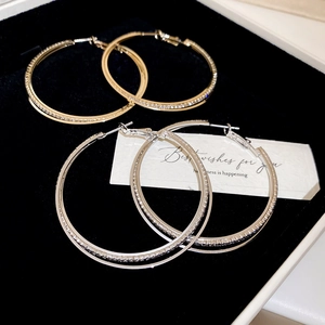Detail of gold and silver double-layered hoop earrings with inlaid zircons on black velvet