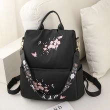 Detailed close-up of pink cherry blossom and butterfly embroidery on black nylon backpack