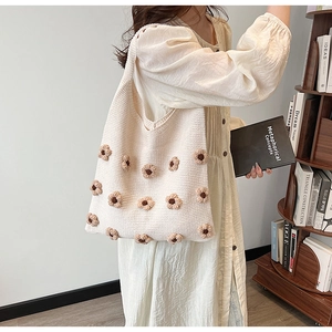 Close-up of cream knitted tote bag featuring 3D flower details in a cozy bookstore setting