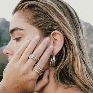 Detail of silver wavy rings and chunky earrings on a model with beach sand textures
