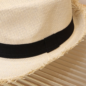 Close-up of beige straw hat texture featuring a raw fringe edge and black ribbon trim