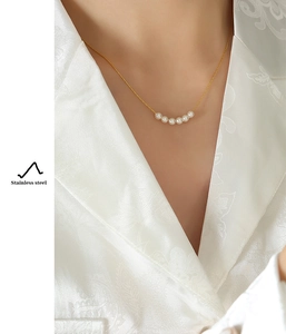 Detail of a gold stainless steel necklace with six small pearls on silk clothing