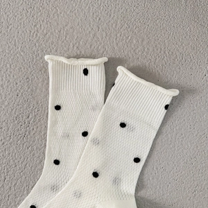 Detail of thin knitted cream socks with black polka dots and ribbed elastic cuffs