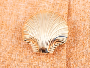 Gros plan sur un bouton en métal doré en forme de coquille sur tissu tweed orange