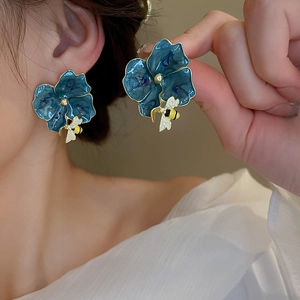 Detail showing a navy blue flower earring with gold edges and a small 3D bee pendant