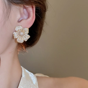 Macro side view of a model wearing gold floral stud earrings with pavé set zircons