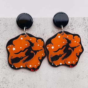 Macro detail of Halloween acrylic earrings featuring an orange witch on broom silhouette