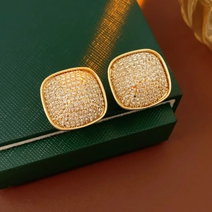 Macro view of gold square stud earrings with pave crystals on a luxury green jewelry box