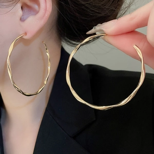 Close-up of a gold twisted hoop earring with a polished metallic texture on a model
