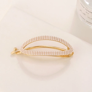 Detailed close-up of a gold metal hair clip with inlaid white pearls and knot design