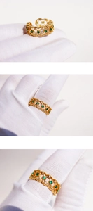 Detail of vintage gold lace ring with emerald zircon stones shown on white gloved hands