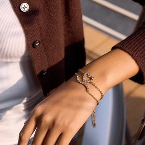 Détail du bracelet double chaîne en acier doré 18K avec cœurs en zircon blanc au poignet