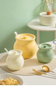 Three ceramic lard pots in yellow, green and white with lids and spoons in kitchen setting