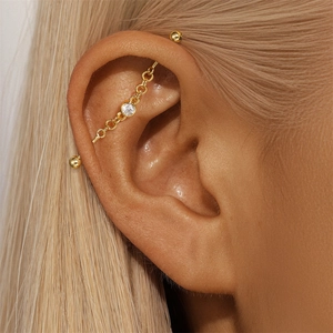 Macro shot of gold industrial barbell piercing with chain and clear zircon stone detail