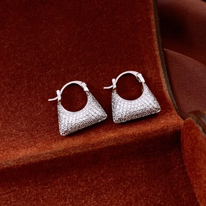 Macro shot of silver geometric earrings with sparkling zircon inlay on red velvet