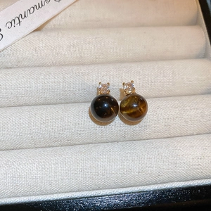 Gros plan de boucles d'oreilles œil de tigre avec pierre brune et sertissage doré