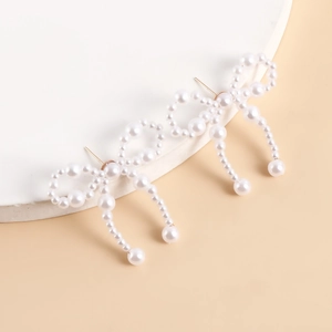 Detail of handcrafted pearl bow earrings with woven tassel design on a display stand