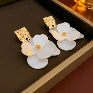 Detailaufnahme goldener Metallblüten und weißer Acrylblumen-Ohrstecker in Nahaufnahme