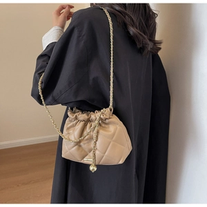 Model wearing a khaki quilted drawstring bucket bag with gold chain and metal ball detail