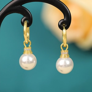 Macro shot of gold pearl drop earrings with sparkling zircon micro-inlay on black stand